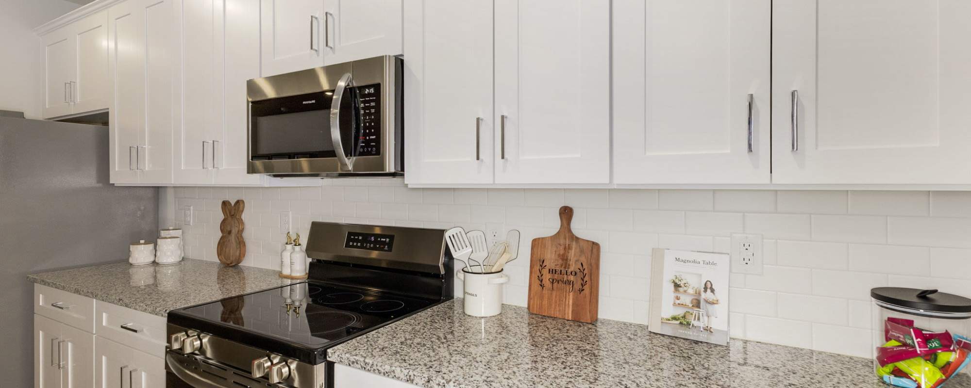 Model kitchen with white cabinetry, custom backsplash, and stainless-steel appliances at The Courts at Maverick Yards in Mauldin, South Carolina