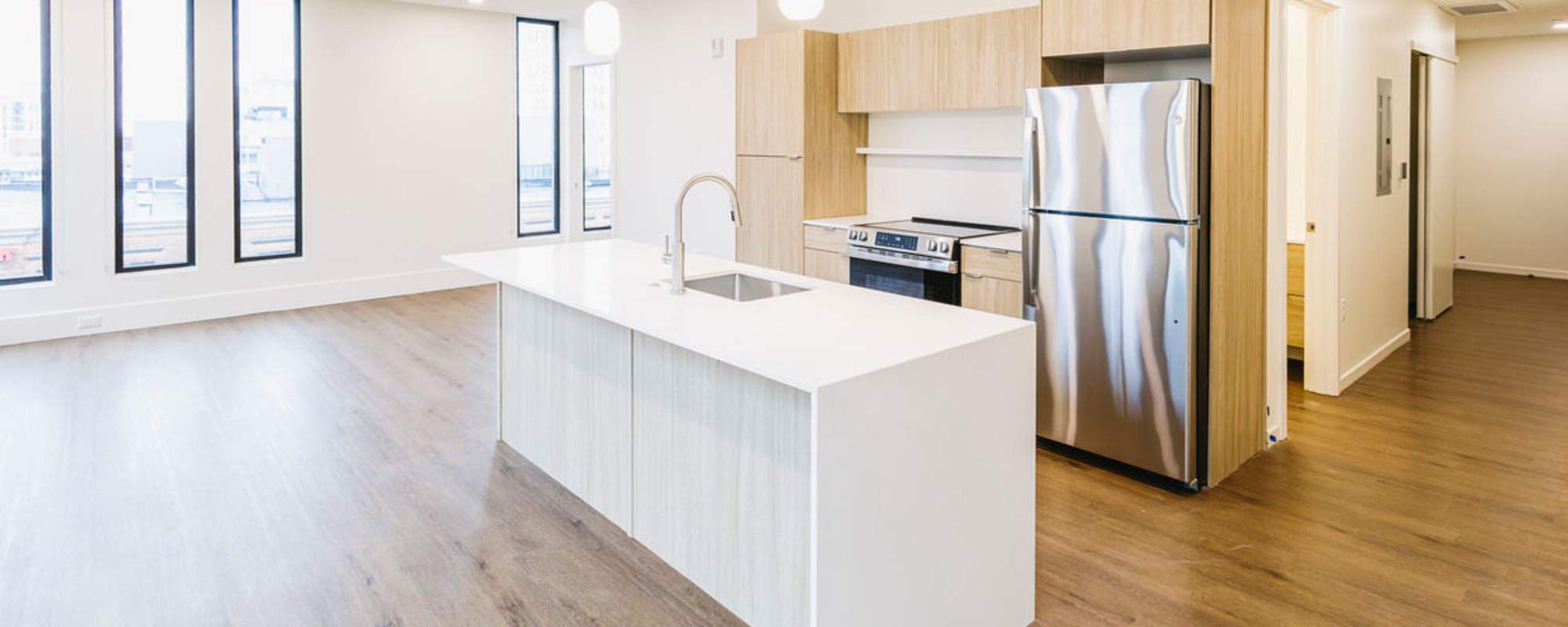 Bright open layout with wood-style flooring, modern kitchen featuring stainless steel appliances and island at Residences at 111 Lyon in Grand Rapids, Michigan
