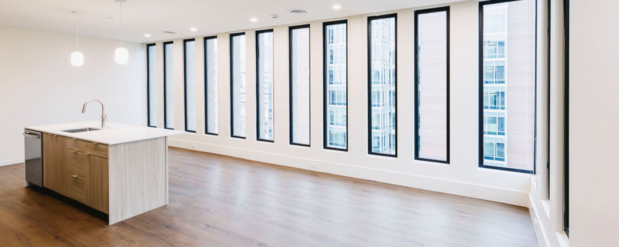 Bright open layout with wood-style flooring and modern kitchen island featuring stainless steel appliances and pendant lights at Residences at 111 Lyon in Grand Rapids, Michigan