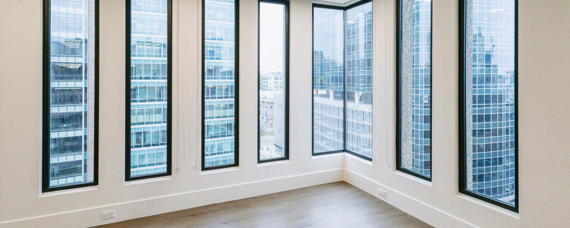 Bright, spacious room with large windows and wood-style flooring, showcasing city views at Residences at 111 Lyon in Grand Rapids, Michigan