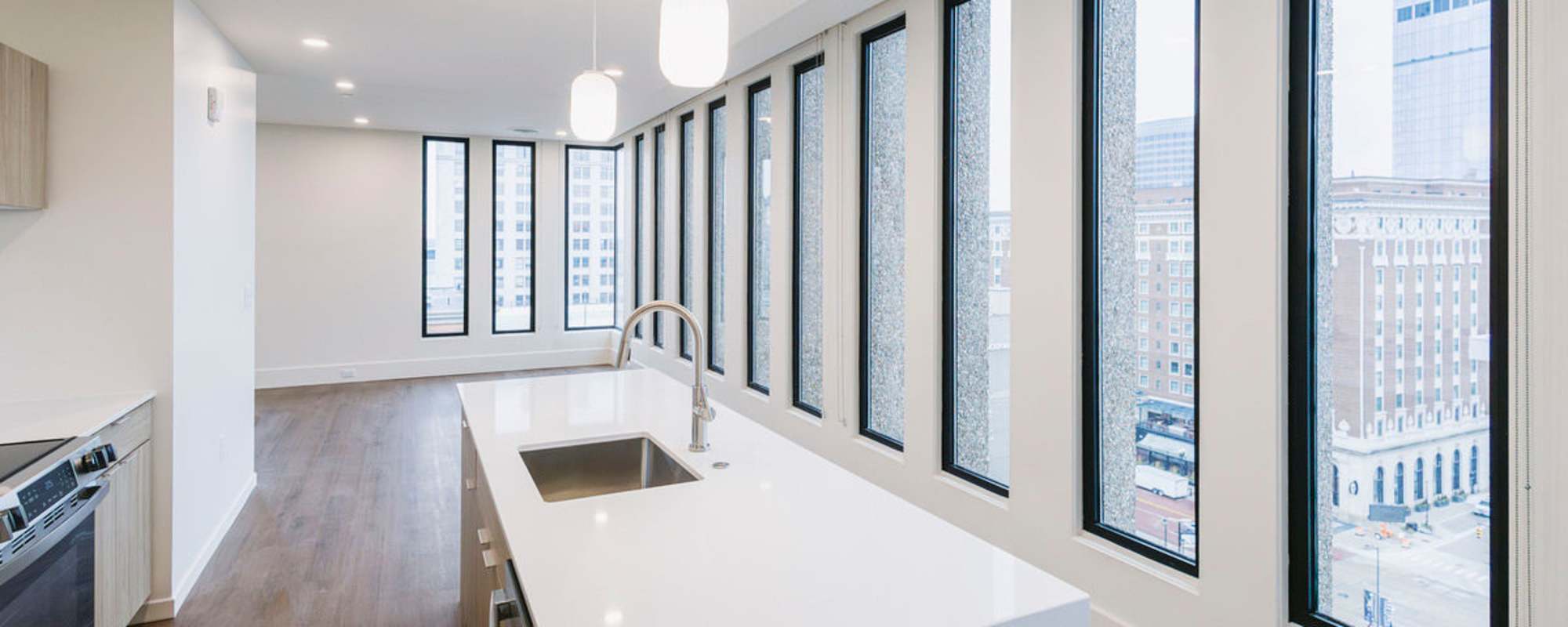 Bright open layout with large windows, modern kitchen featuring white countertops and stainless steel appliances, wood-style flooring at Residences at 111 Lyon in Grand Rapids, Michigan