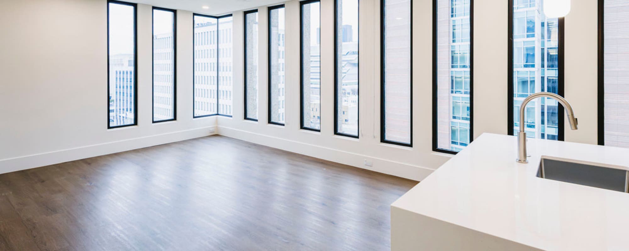 Spacious apartment with large windows and wood-style flooring, featuring a modern kitchen island at Residences at 111 Lyon in Grand Rapids, Michigan