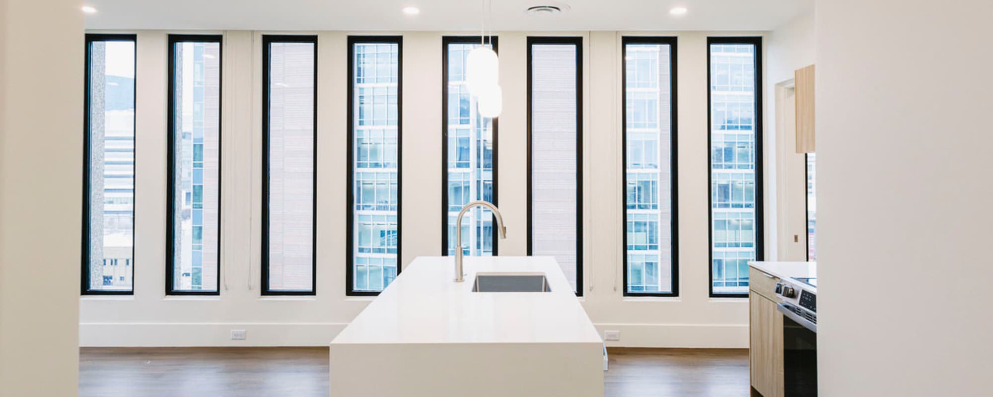 Bright kitchen with island, stainless steel appliances, large windows, and wood-style flooring at Residences at 111 Lyon in Grand Rapids, Michigan