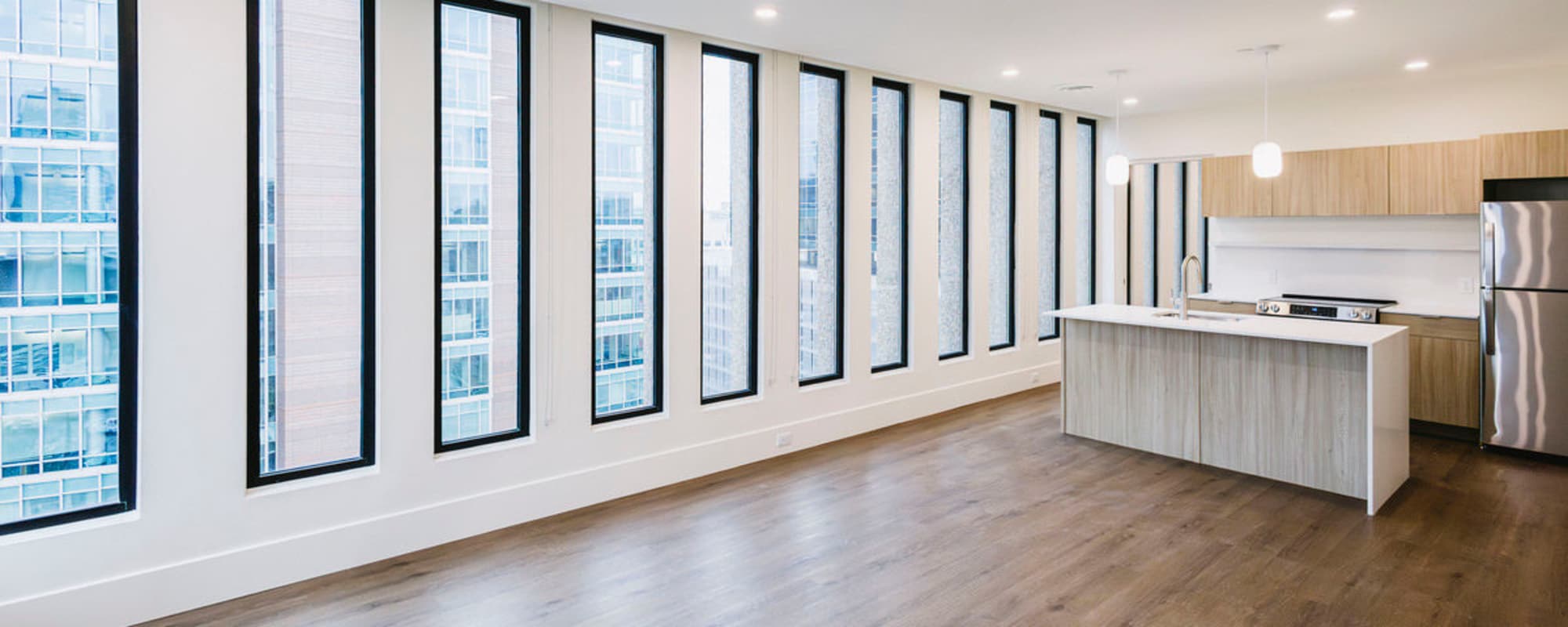 Bright open layout with large windows, wood-style flooring, and modern kitchen featuring stainless steel appliances and island at Residences at 111 Lyon in Grand Rapids, Michigan