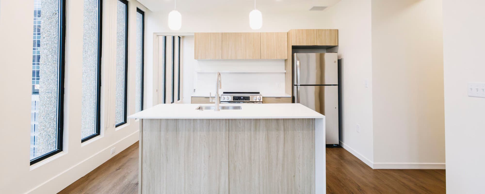 Modern kitchen with granite countertops, stainless steel appliances, and wood-style flooring, featuring large windows for natural light at Residences at 111 Lyon in Grand Rapids, Michigan