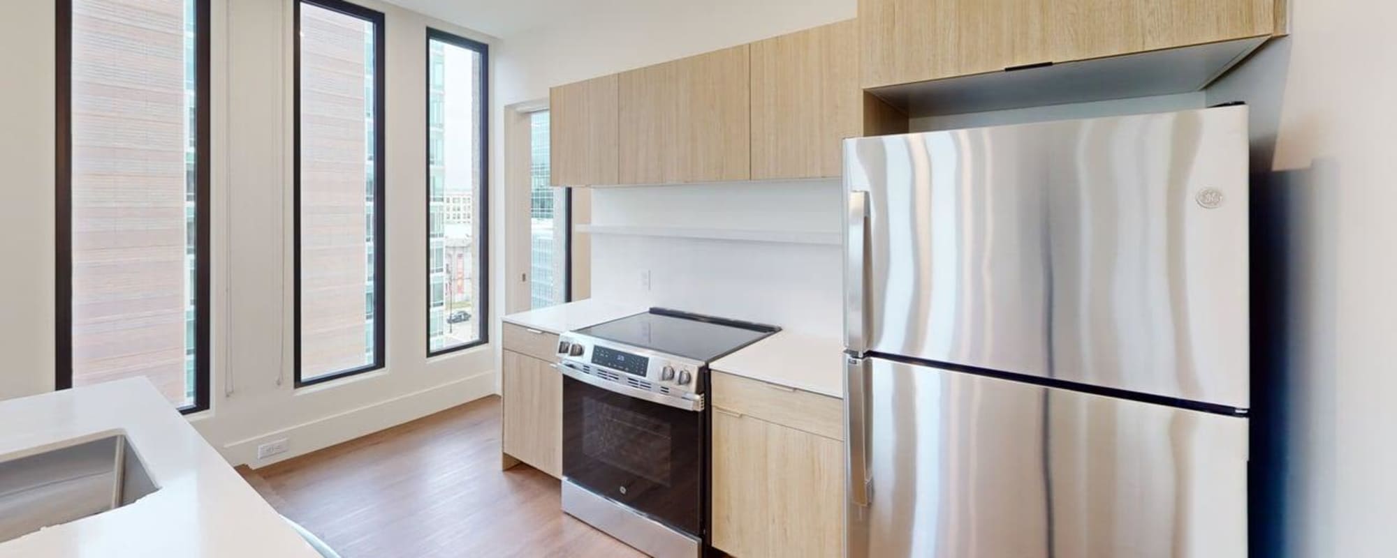 Modern kitchen with stainless steel appliances, granite countertops, and wood-style flooring, featuring large windows at Residences at 111 Lyon in Grand Rapids, Michigan