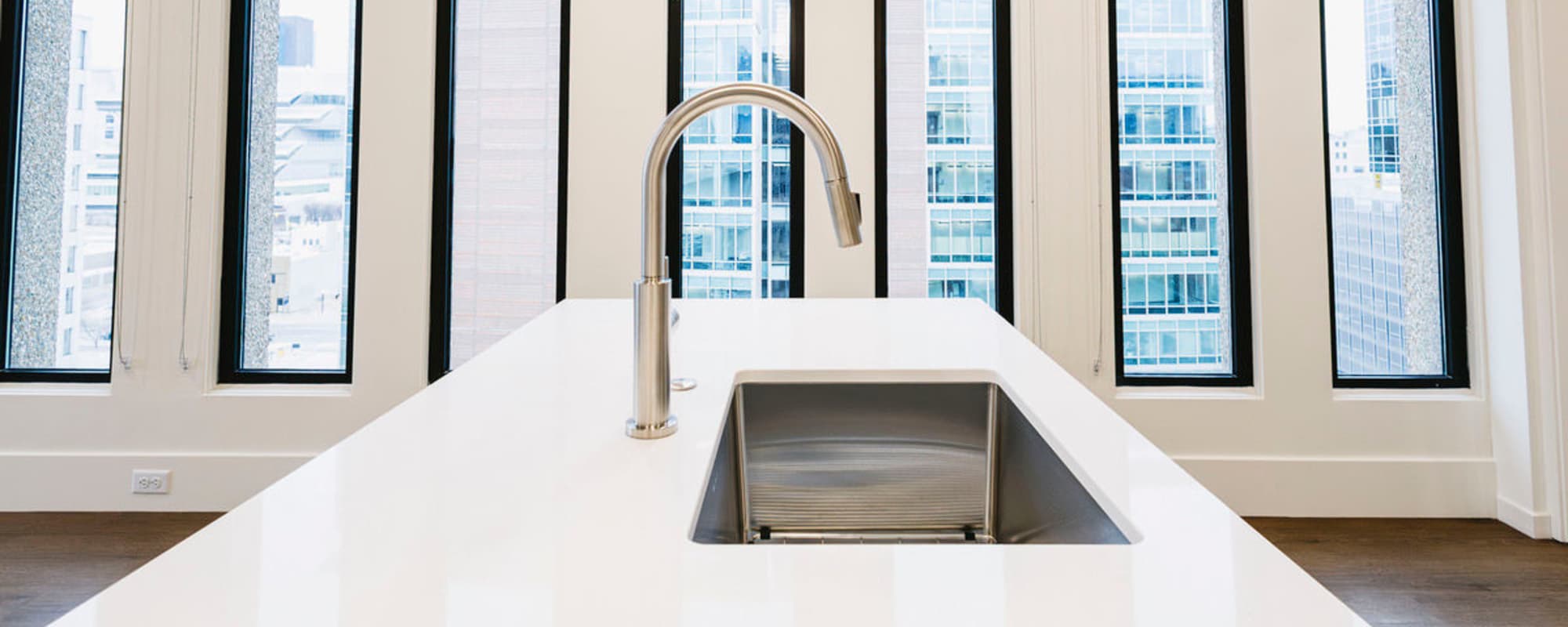 Modern kitchen with white countertops, stainless steel faucet, and large windows showcasing city views at Residences at 111 Lyon in Grand Rapids, Michigan