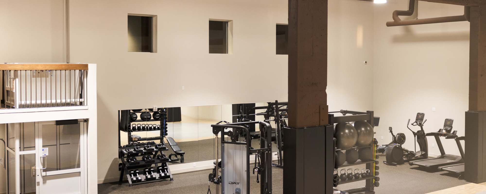 Modern fitness center with weight racks, cable machines, cardio equipment, and mirrored wall in an open loft-style space at Residences at 111 Lyon in Grand Rapids, Michigan