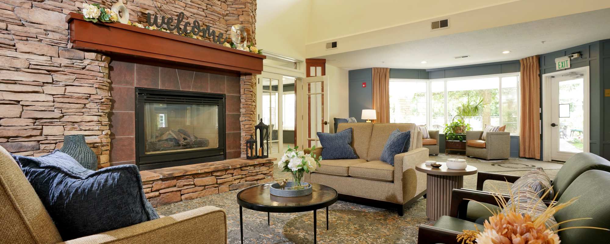 Cozy community lounge with stone fireplace, sofas, and natural light at The Wellington in Salt Lake City, Utah