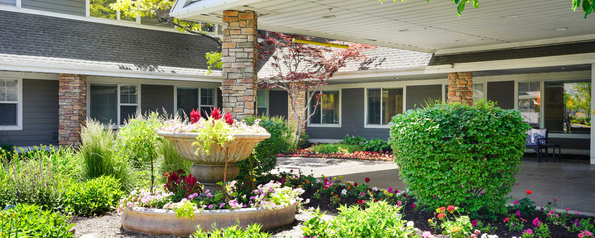 Community entrance with covered porch, stone pillars, and flower garden fountain at The Wellington in Salt Lake City, Utah