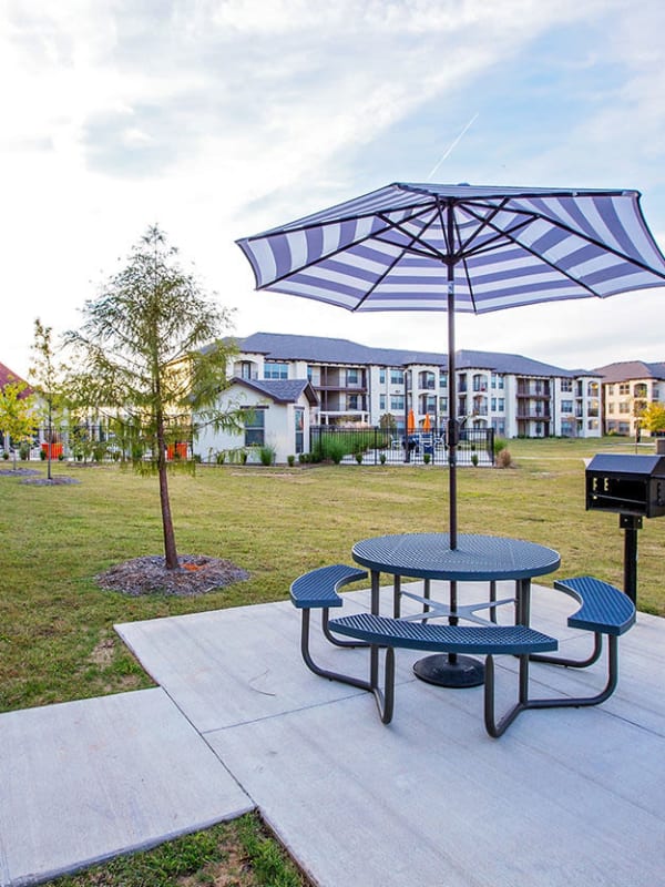 Outdoor picnic table with umbrella and manicured grounds at Palisades at Pleasant Crossing in Rogers, Arkansas