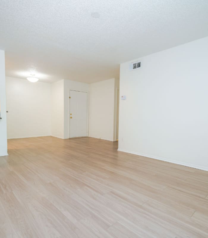 Empty living room with wood-look flooring, entry door and kitchen opening at Huntington Reserve in Sanford, Florida