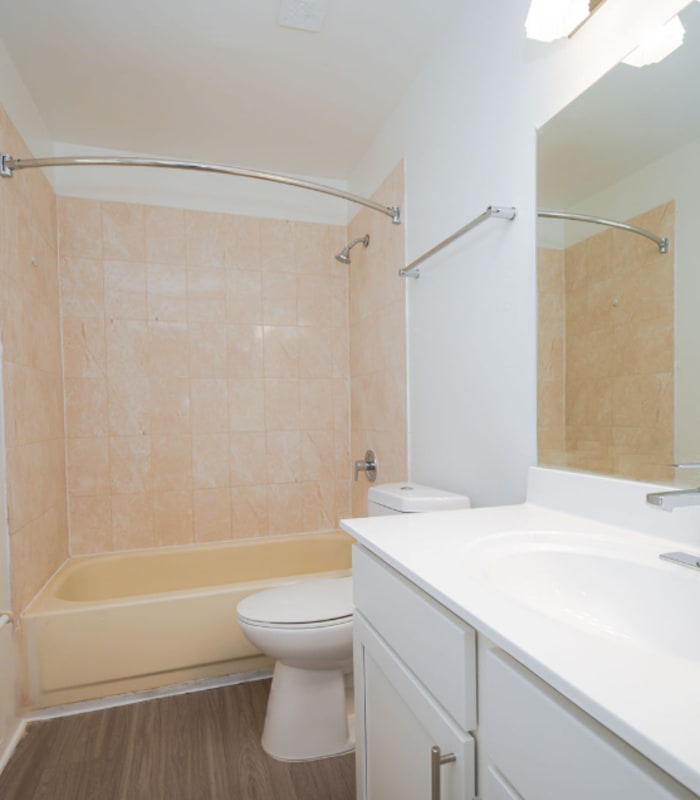 Bathroom with tan tile tub surround, toilet and white vanity with mirror at Huntington Reserve in Sanford, Florida