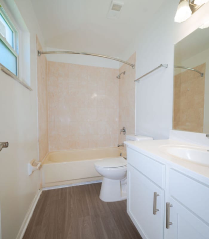 Bathroom with tan tile tub surround, toilet and white vanity with mirror at Huntington Reserve in Sanford, Florida
