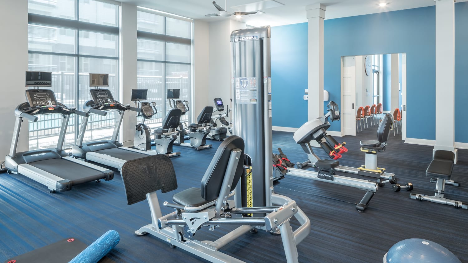 Fitness center at our over 55 apartments in Lakewood, CO, featuring exercise equipment, weights, and large windows. 