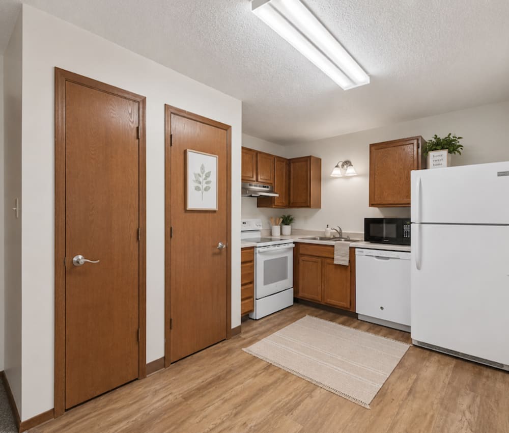 Bright kitchen with white appliances, wood-style flooring, and cozy dining area with round table and chairs at Riverbirch in Ames, Iowa