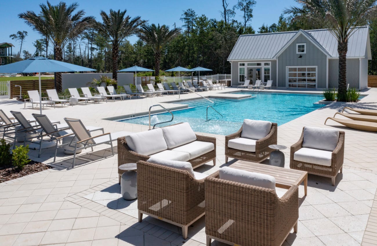 Luxury Apartments Ponte Vedra Beach, FL - Cadence at Nocatee - Resort-Inspired Swimming Pool Surrounded by Palm Trees with Lounge Chairs and Tables.