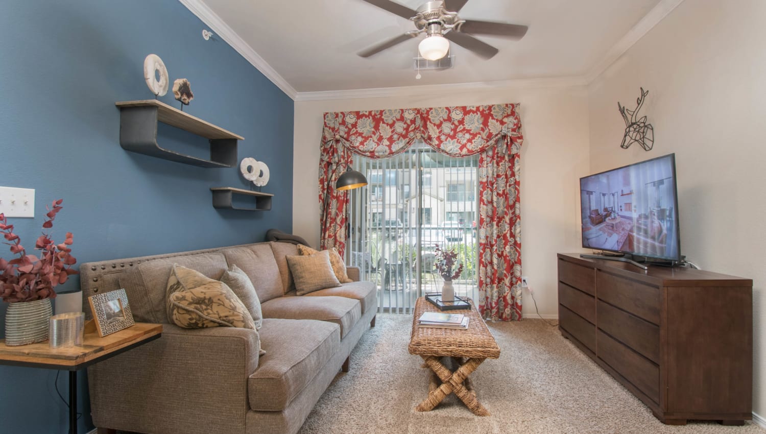 Accent wall and a ceiling fan in the comfortably furnished living area of a model apartment at Carrington Oaks in Buda, Texas