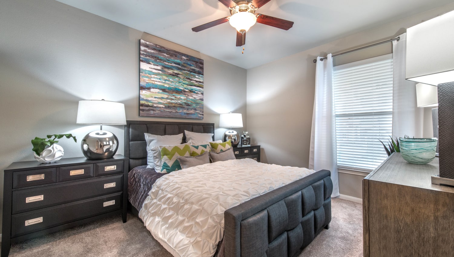 Comfortably furnished bedroom with a ceiling fan in a model apartment at Olympus Las Colinas in Irving, Texas