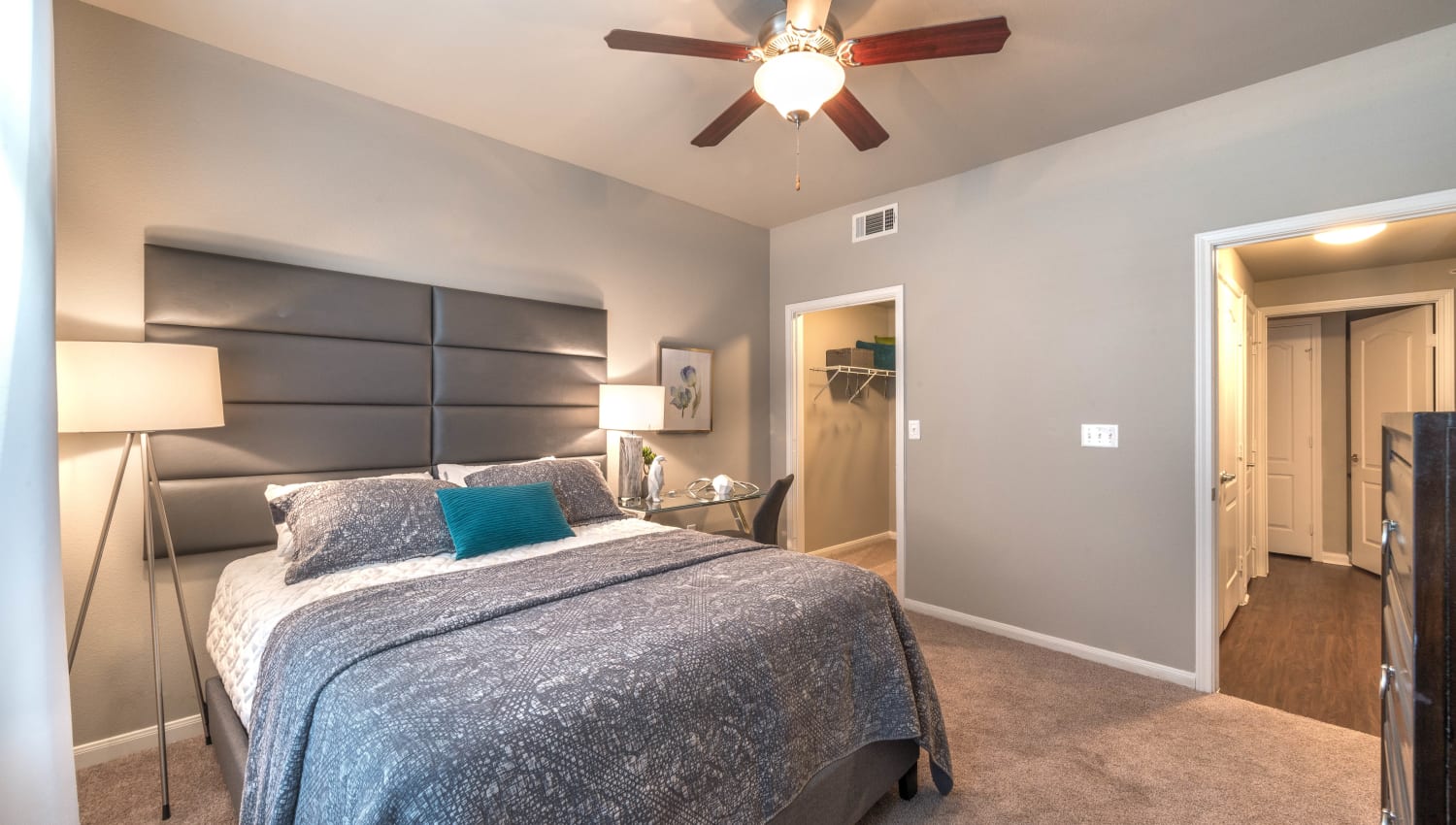 Model home's master bedroom with a walk-in closet and a ceiling fan at Olympus Las Colinas in Irving, Texas