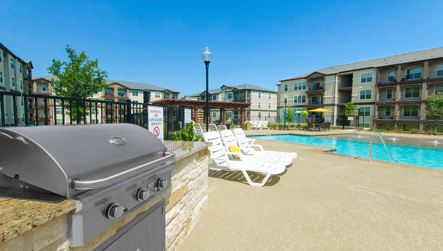 Barbecue area with gas grills near the pool at Olympus Woodbridge in Sachse, Texas