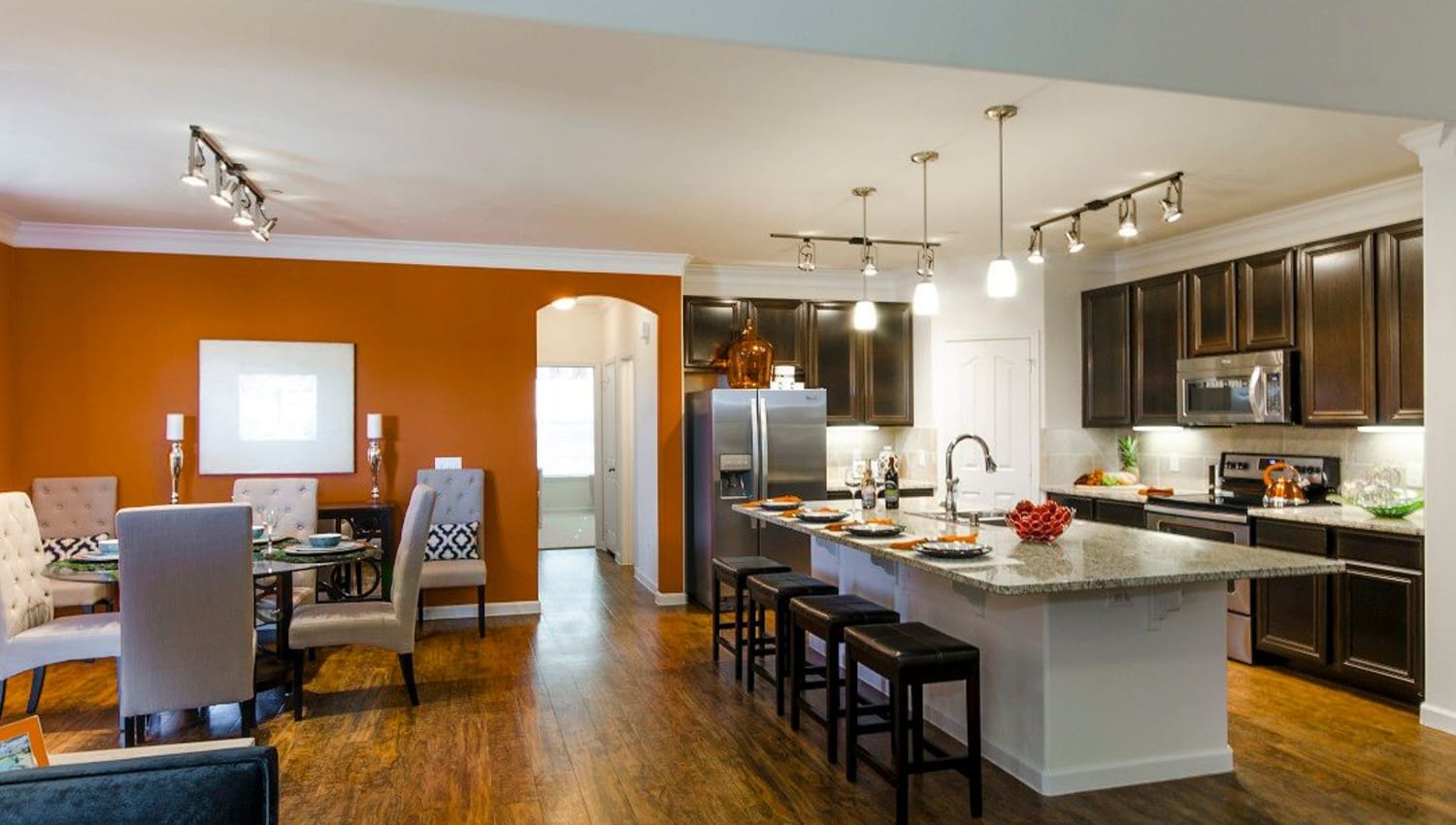 Gorgeously designed open-concept living and kitchen areas with an accent wall and hardwood floors in a model apartment at Olympus Woodbridge in Sachse, Texas 