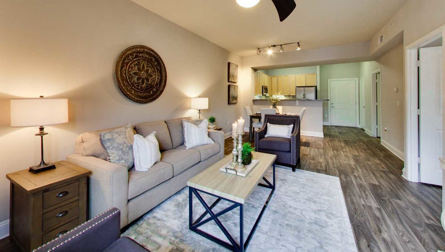 Model living room with contemporary plank flooring and a ceiling fan in an open concept apartment home at SouthPark Morrison in Charlotte, North Carolina