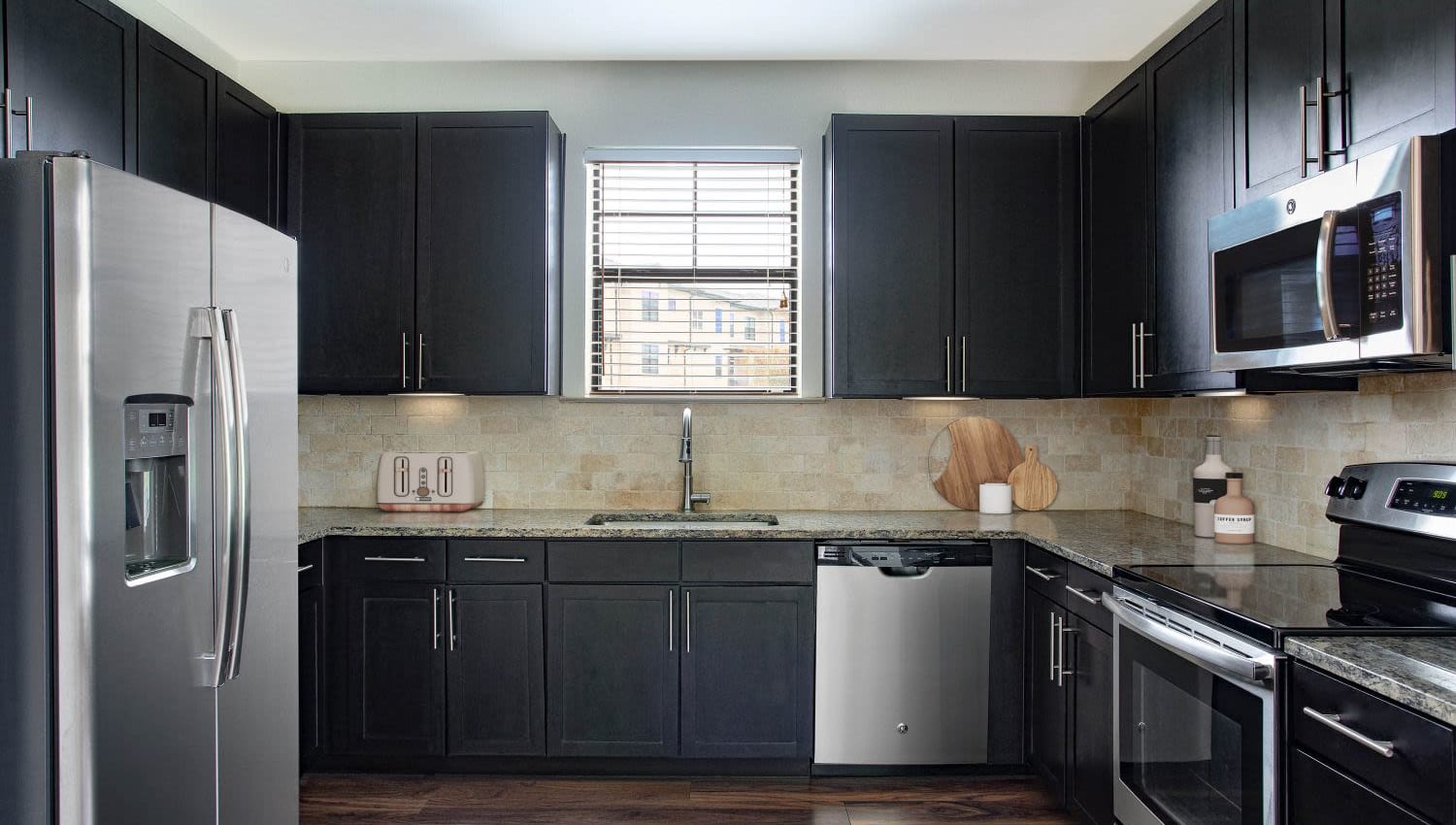 Kitchen with dark wood cabinets and granite countertops at Olympus Falcon Landing in Katy, Texas