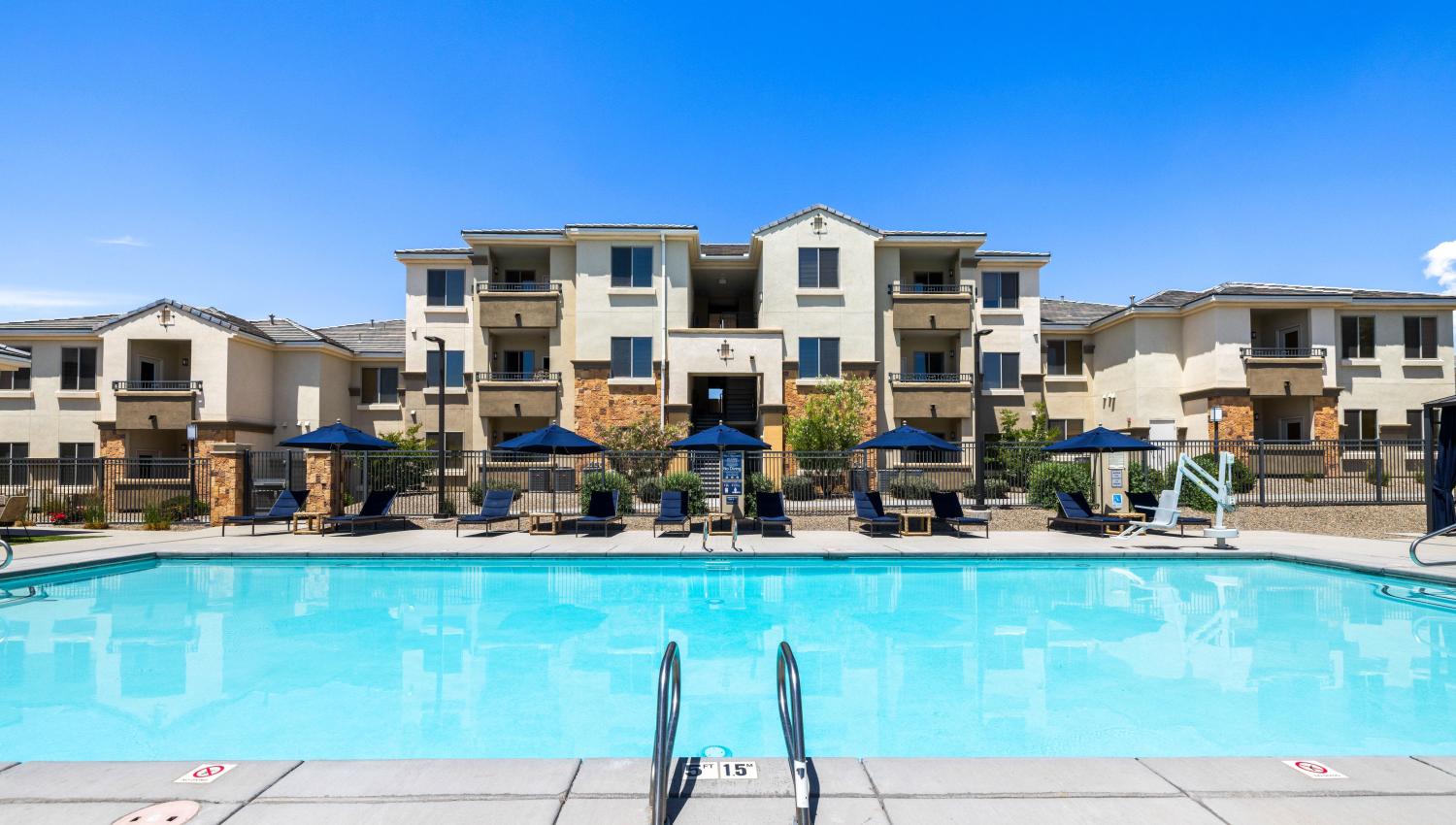 A pool with chairs and umbrellas in front of a building at Olympus Alameda in Albuquerque, New Mexico