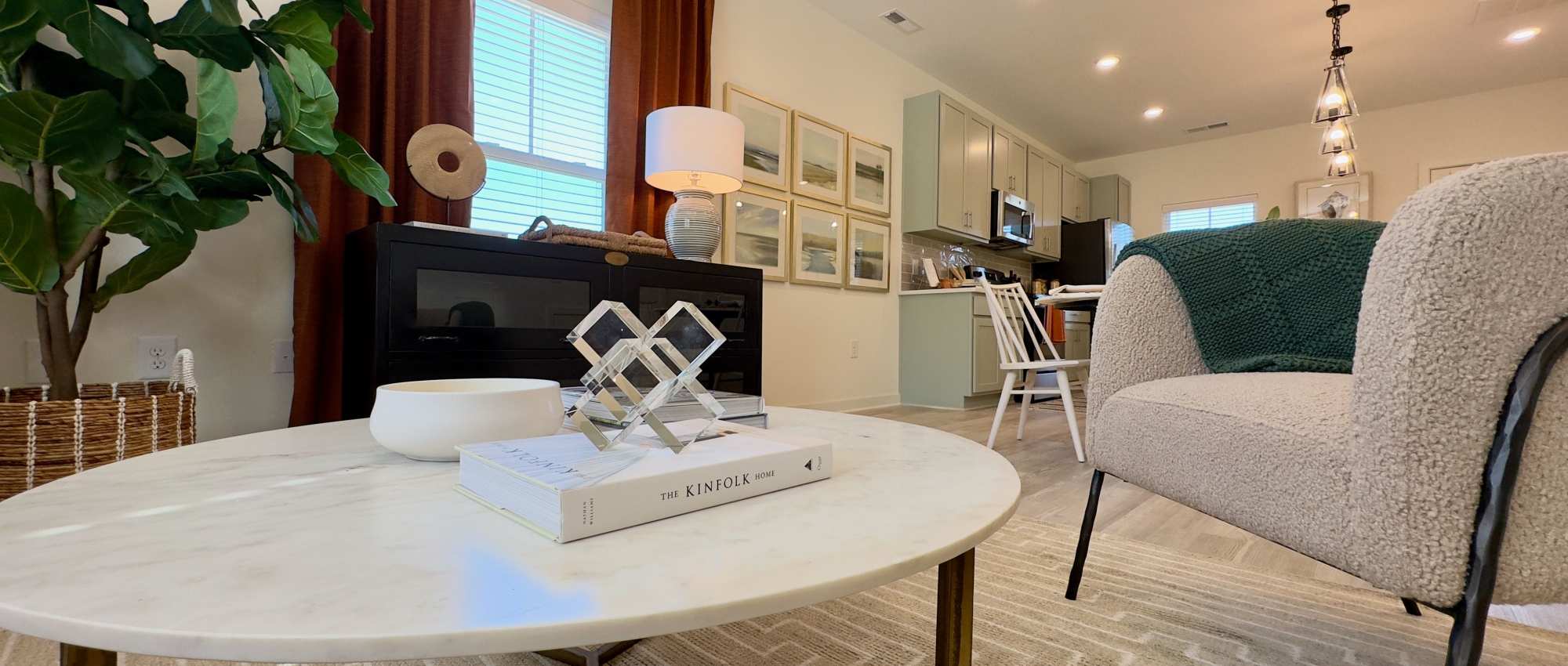 Cozy living room with wood-style flooring, modern decor, and a fully-equipped kitchen in the background at Encore at Westgate in Leland, North Carolina