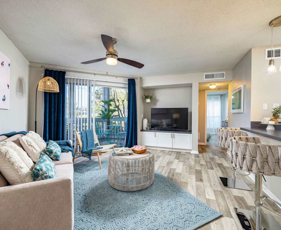 Open layout living room with wooden flooring, couch, television and access to balcony at Lofton Place in Tampa, Florida