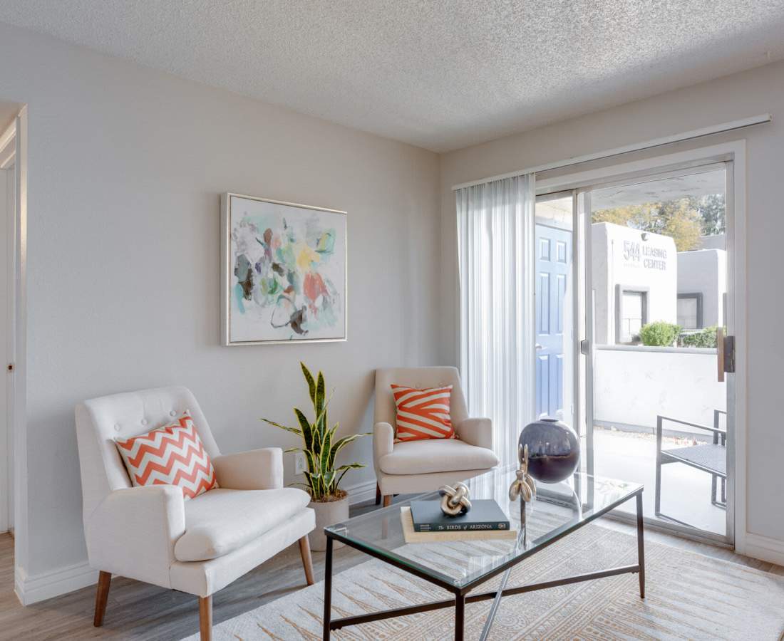 Living room with arm chairs, coffee table and access to private balcony at 544 Southern Apartments in Mesa, Arizona