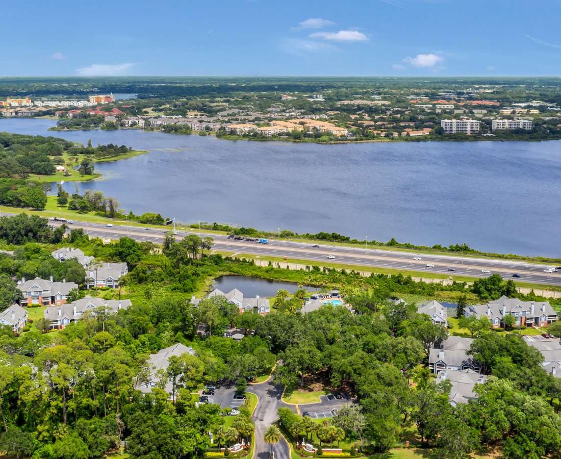 Aerial view of the apartment complex situated amidst lush greenery and alongside a tranquil lake at Rosemont Windermere in Orlando, Florida