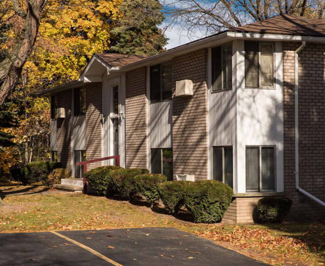 Two-story apartment building with brick exterior, surrounded by landscaped greenery and autumn leaves at Presidential Estates in Rochester, New York