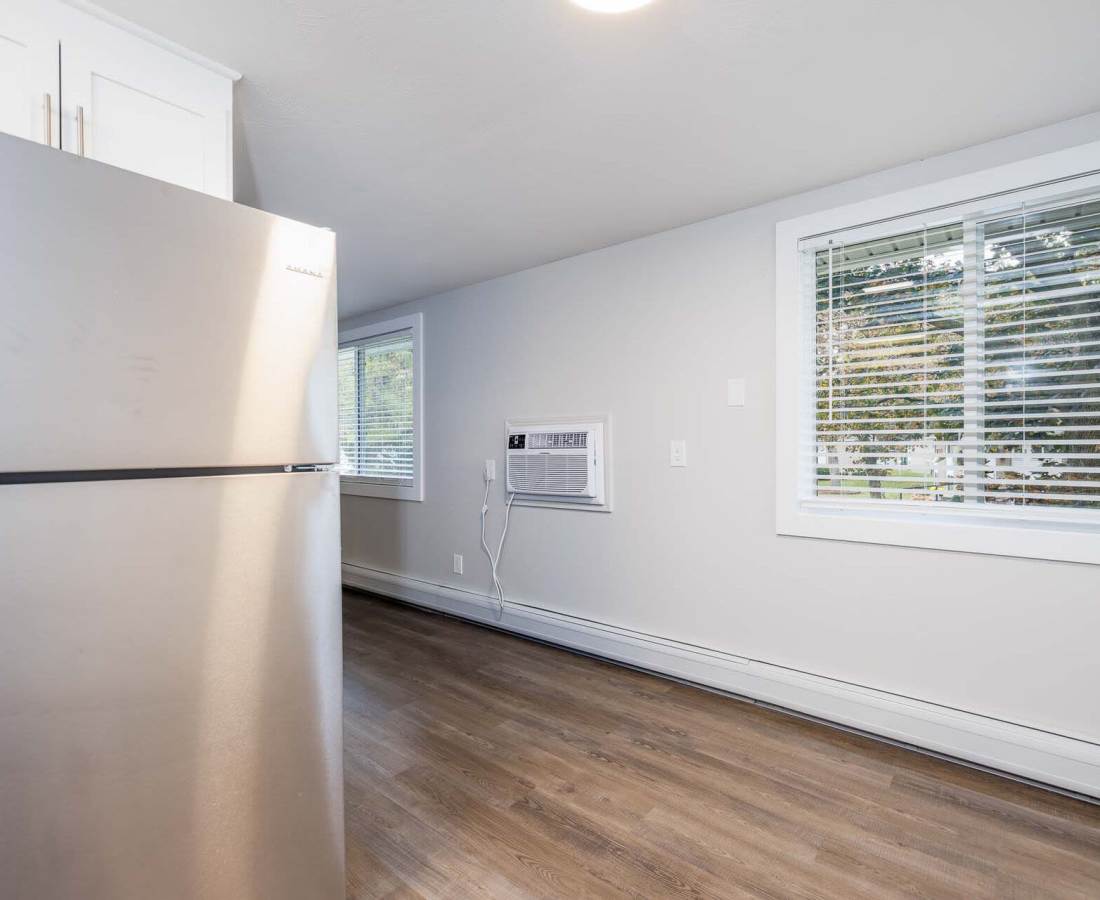 Modern kitchen with stainless steel refrigerator, wood-style flooring, and bright window with blinds at Presidential Estates in Rochester, New York