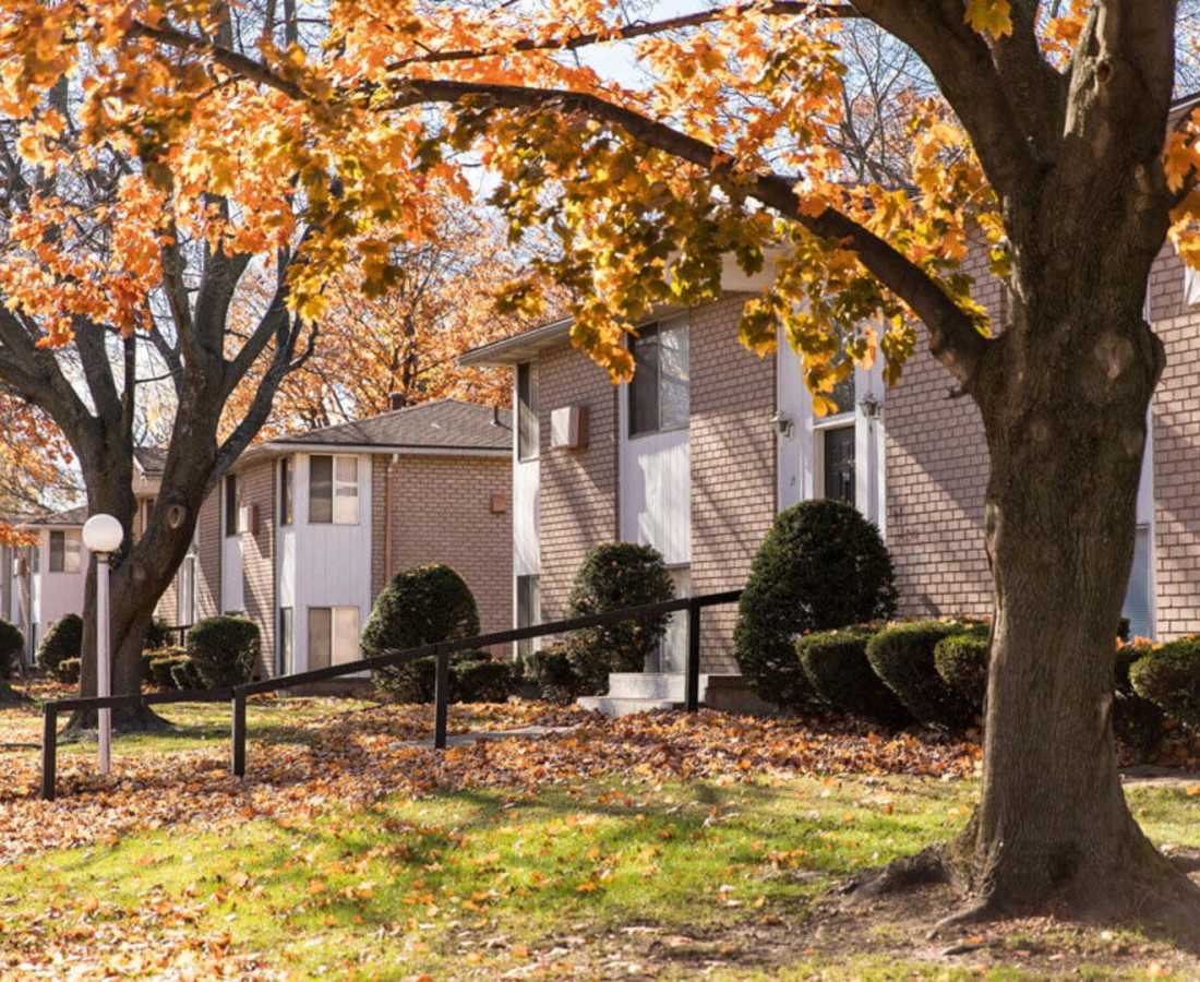Autumn leaves surround brick apartment buildings with manicured shrubs and a gentle slope to the entrance at Presidential Estates in Rochester, New York
