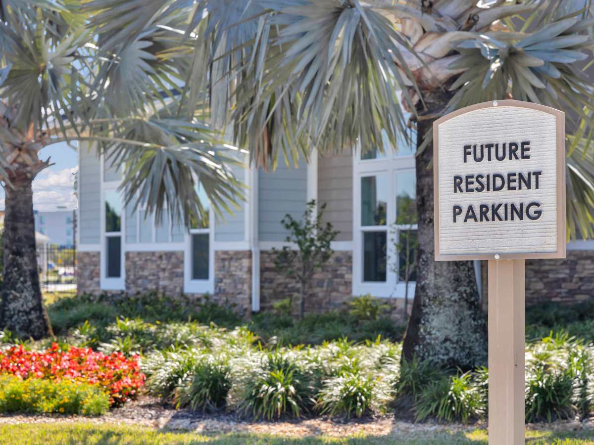 Sign for future resident parking with landscaped greenery and palm trees in the background at The Carlton of West Melbourne in West Melbourne, Florida