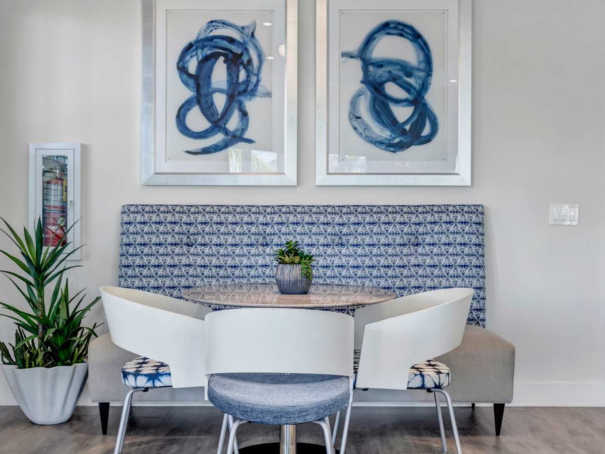 Bright dining area with patterned seating, modern table, and potted plants, featuring stylish artwork on the walls at The Carlton of West Melbourne in West Melbourne, Florida