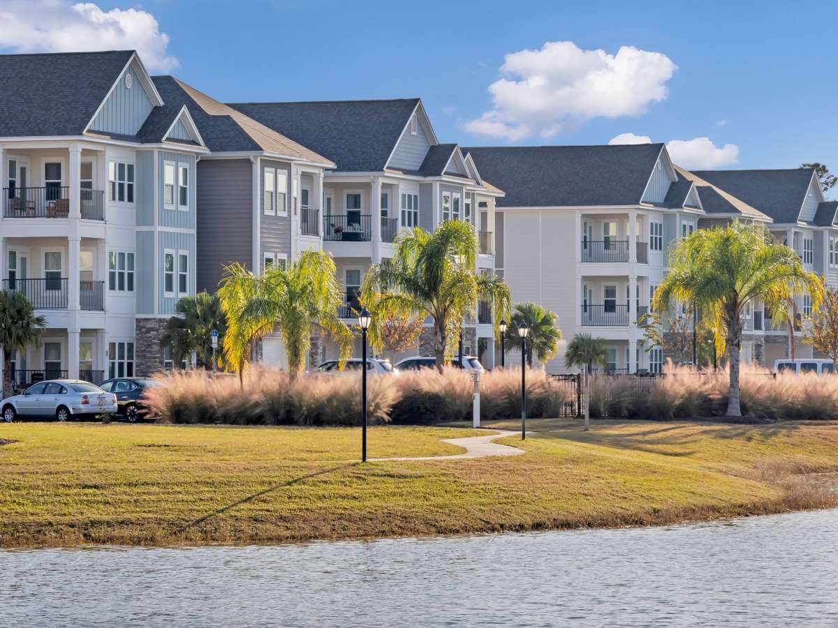 Modern apartment community with palm trees, water view, and well-maintained landscaping at The Carlton of West Melbourne in West Melbourne, Florida