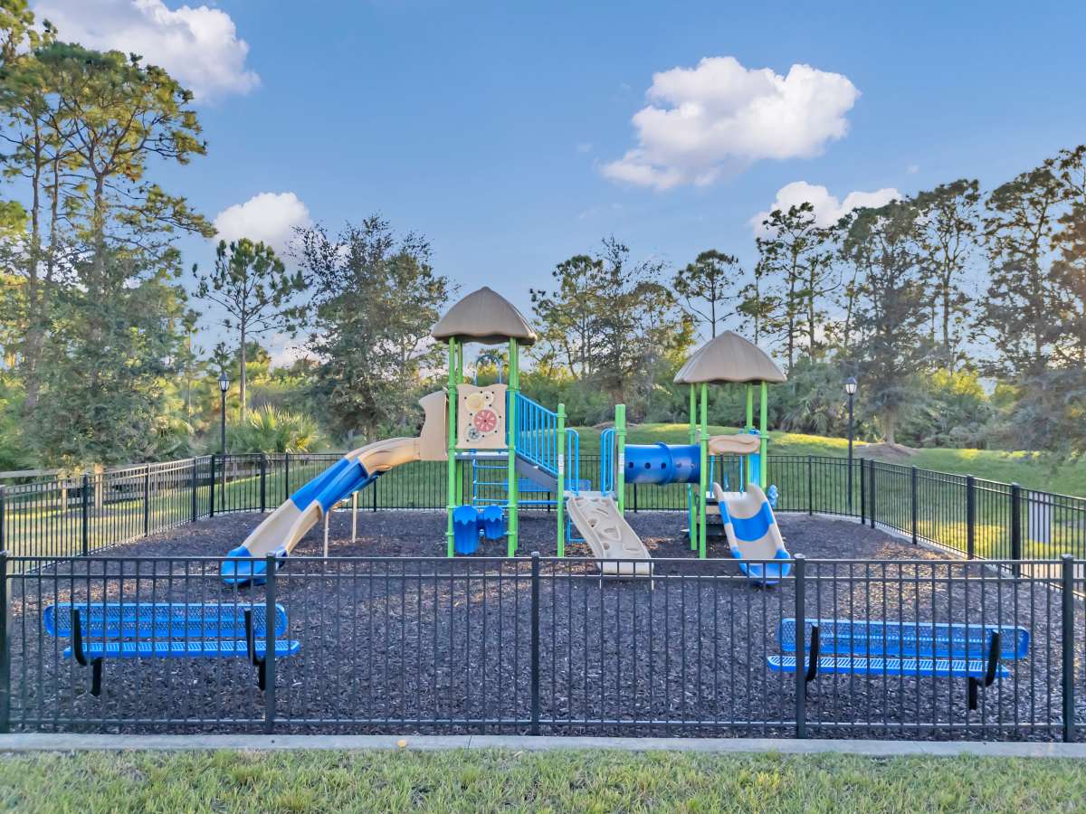 Colorful playground with slides and climbing structures, surrounded by a black fence and green grass at The Carlton of West Melbourne in West Melbourne, Florida