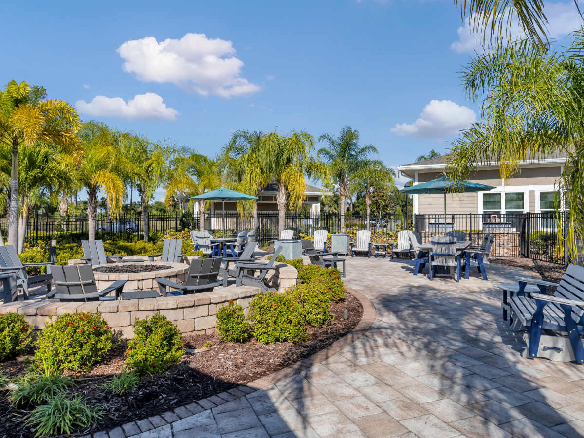 Resort-style outdoor lounge area with seating, fire pit, and lush palm trees at The Carlton of West Melbourne in West Melbourne, Florida