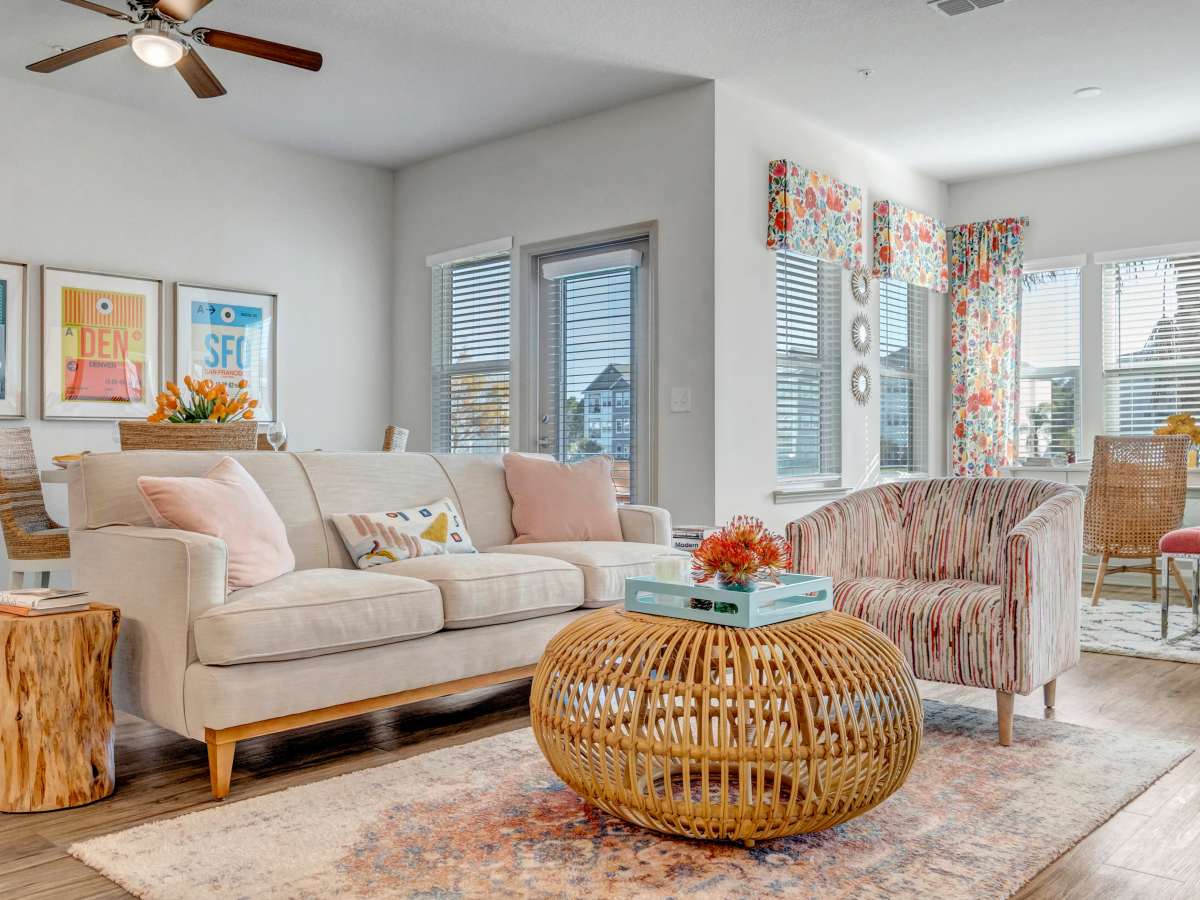 Bright living room with wood-style flooring, cozy sofa, colorful decor, and large windows at The Carlton of West Melbourne in West Melbourne, Florida