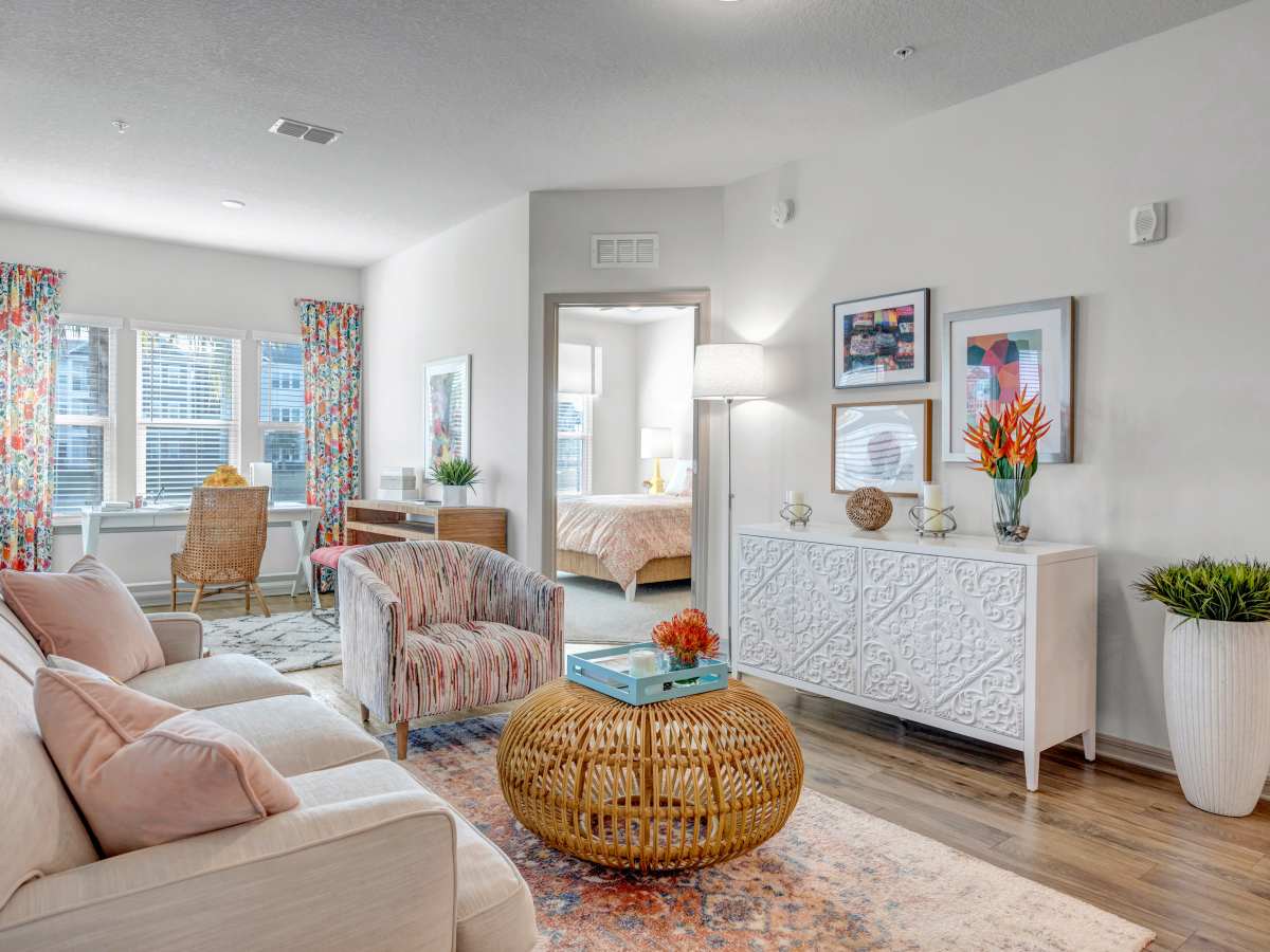 Bright living area with wood-style flooring, colorful curtains, and modern decor, featuring a cozy sofa and accent chairs at The Carlton of West Melbourne in West Melbourne, Florida