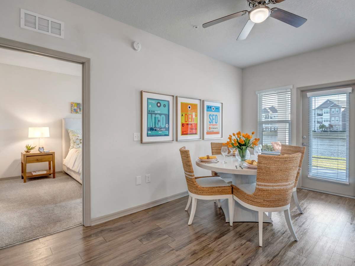 Bright dining area with round table, woven chairs, and large windows overlooking water at The Carlton of West Melbourne in West Melbourne, Florida