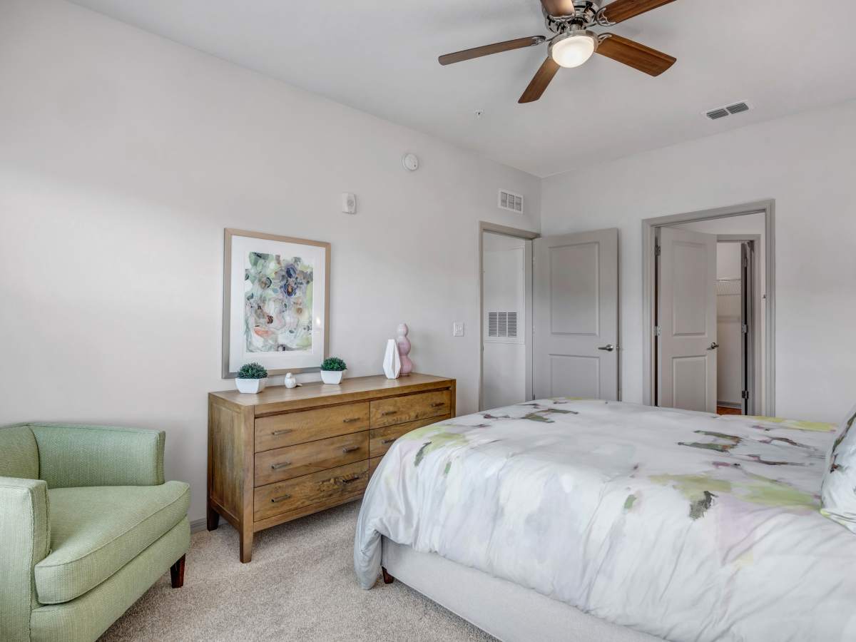 Bright bedroom with plush carpet, green accent chair, wooden dresser, and colorful wall art at The Carlton of West Melbourne in West Melbourne, Florida