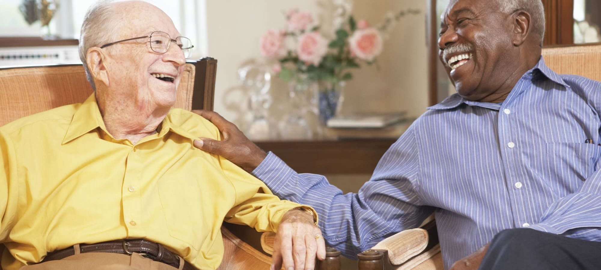 Two men sitting and smiling at one another, one in yellow shirt and one in blue.