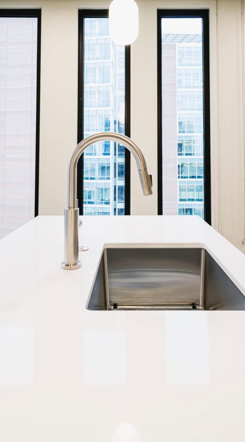 Kitchen island with white countertop, modern sink, and city views through tall narrow windows at Residences at 111 Lyon in Grand Rapids, Michigan