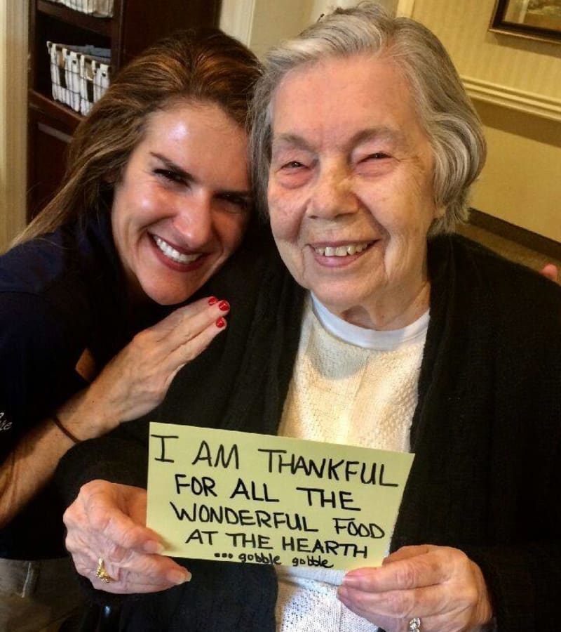 A caretaker and resident smiling, holding a piece of paper that says 'I am thankful for all the wonderful food at the hearth'