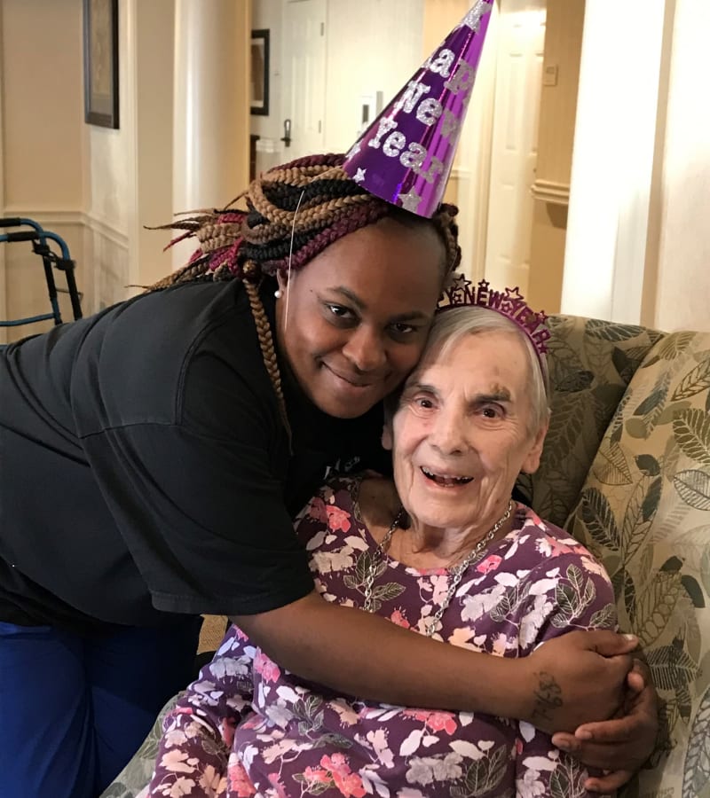Caretaker wearing a cone-shaped 'happy new year' hat hugging a seated resident at a Hearth Management community