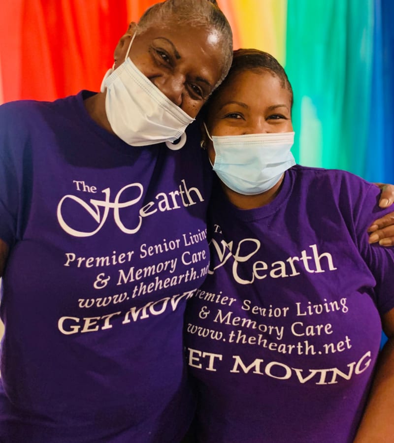 Two hearth employees hugging in front of a rainbow banner at a Hearth Management community